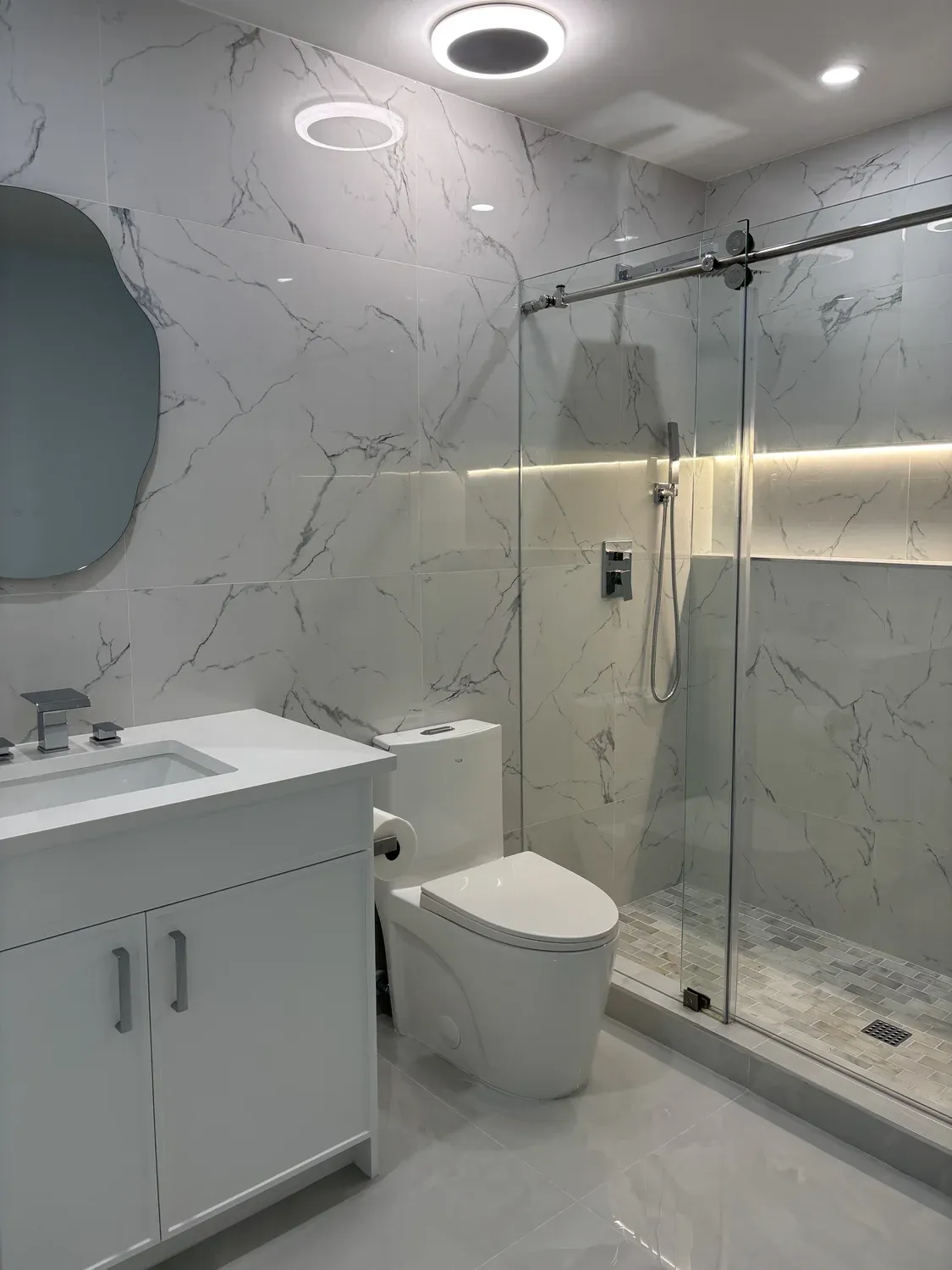 Marble bathroom with organic-shaped mirror and glass shower